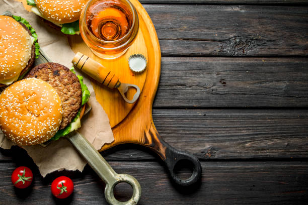 istock Burgers on paper with beer and tomatoes. 1144172208
