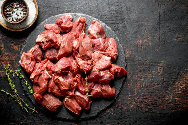 Photo of Cut raw beef on a stone Board with thyme and seasonings in bowls.