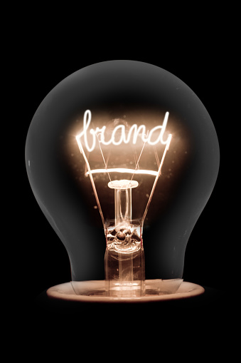 Photo of single light bulb with shining fiber in BRAND shape isolated on black background