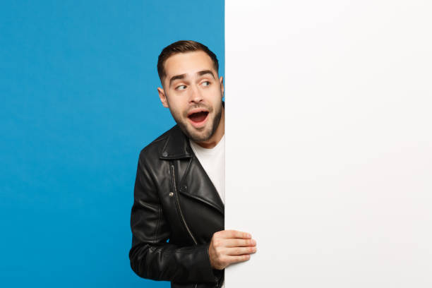 istock Handsome young unshaven man hold big white empty blank billboard for promotional content isolated on blue wall background studio portrait. People sincere emotions lifestyle concept. Mock up copy space 1144186663