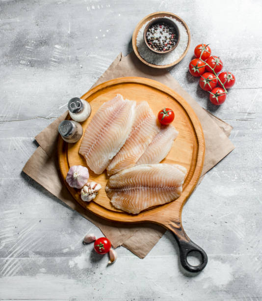 istock Fish fillet on a round cutting Board with spices, tomatoes and garlic. 1144187954