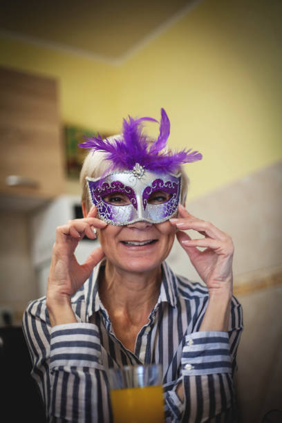 Senior hispanic grey- haired woman wearing venetian carnival mask smiling in love doing heart symbol shape with hands. romantic concept.
