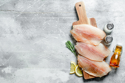 Fish fillet on a cutting Board with lemon slices, spices and oil in a bottle. On white rustic background