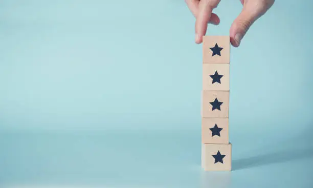 Photo of Woman Hand putting wooden five star shape on blue background.