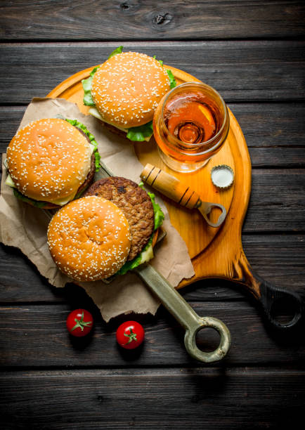 istock Burgers on paper with beer and tomatoes. 1144189598
