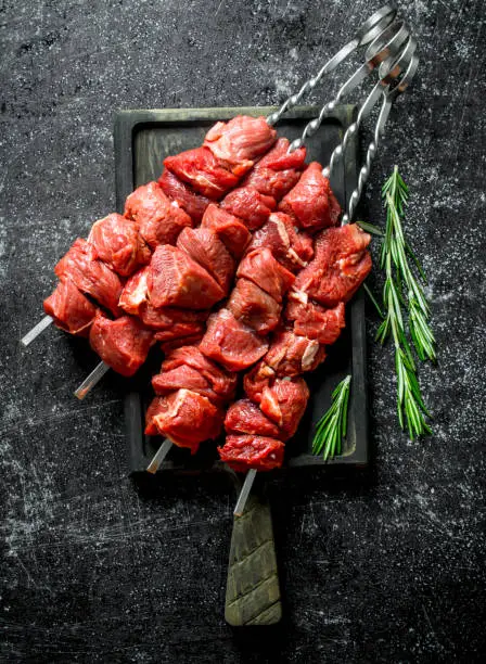 Photo of Raw kebab on a cutting Board with rosemary.