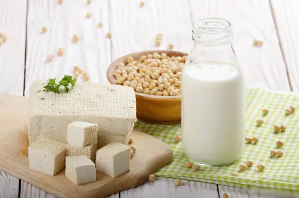 Non-dairy alternatives Soy milk or yogurt in glass bottle and tofu on white wooden table with soybeans in bowl aside