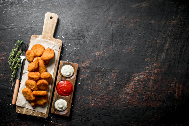 istock Chicken nuggets on a cutting Board with thyme and sauces. 1144194036