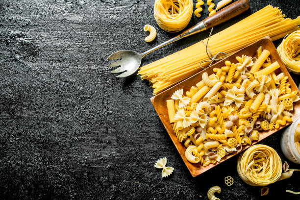 Assortment of different types of dry pasta on a plate with ladle. Assortment of different types of dry pasta on a plate with ladle. On black rustic background carbohydrate food type photos stock pictures, royalty-free photos & images