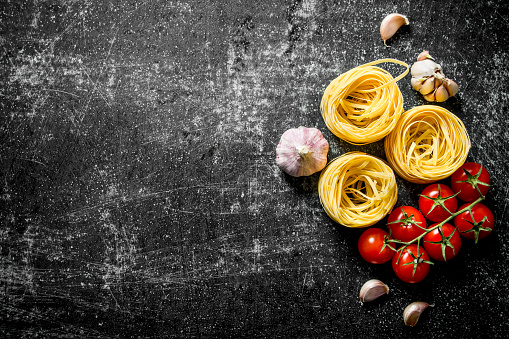 Raw tagliatelle paste with garlic and tomatoes. On black rustic background