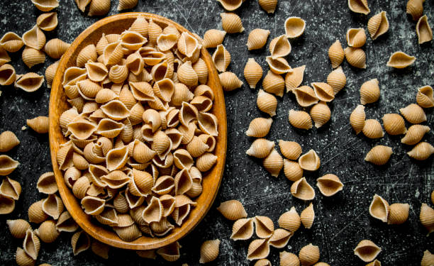 istock Pasta background. Dry pasta conchille in bowl. 1144196318