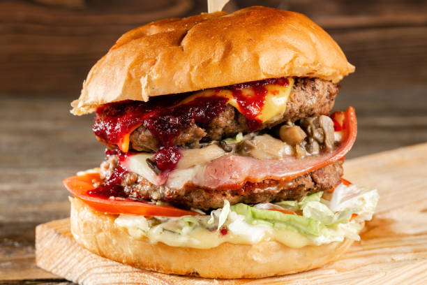 istock A big burger with two beef cutlets, cooked on charcoal. Lunch on a wooden background. The concept of fast food and not healthy food 1144200992