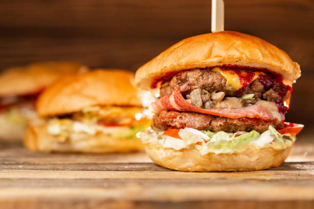 istock Three big burger with meat cooked on BBQ coal. Lunch on a wooden background. The concept of fast food and unhealthy food 1144201021