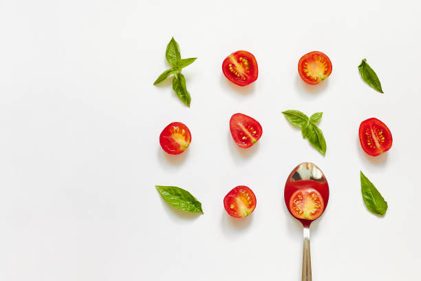 tomate rojo cereza, hojas de albahaca verde y cuchara sobre fondo blanco - tomate cereza fotografías e imágenes de stock