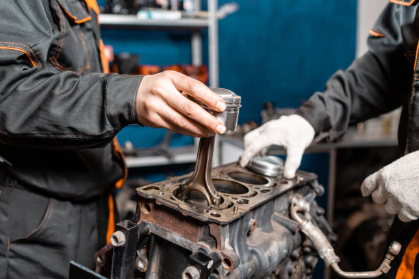 istock Two mechanic holding a new piston for the engine, overhaul.. Engine on a repair stand with piston and connecting rod of automotive technology. Interior of a car repair shop. 1144203560