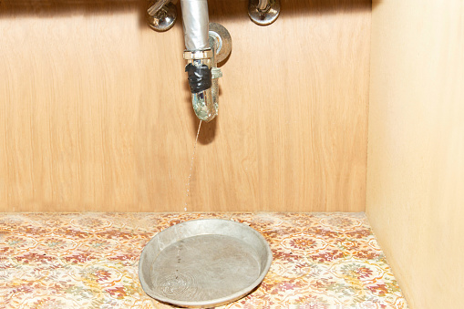 horizontal image of water running out of a broken and rusted out pipe underneath the bathroom sink