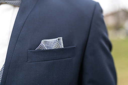 View to the male coat pocket with a fixed white square. Men's suit accessories. Wedding male guest's attire. Male wedding style. Formal dinner outfit for men. Elements of suit. Pocket square folding