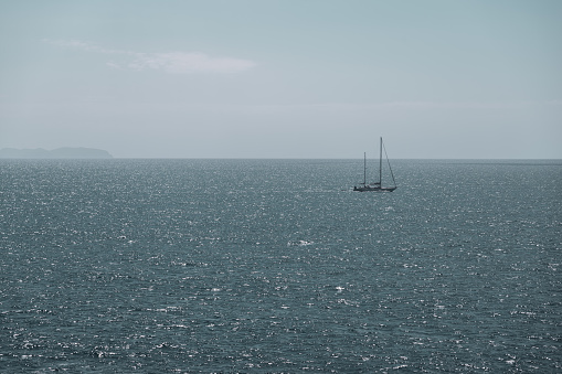 Horizon over open water, off the southern coast of Mallorca, at Cala Pi, Spain.  Yacht crossing the field of vision in the distance.  To the left hand side, through the haze, is the outline of the island of Cabrera (a natural park and marine reserve).