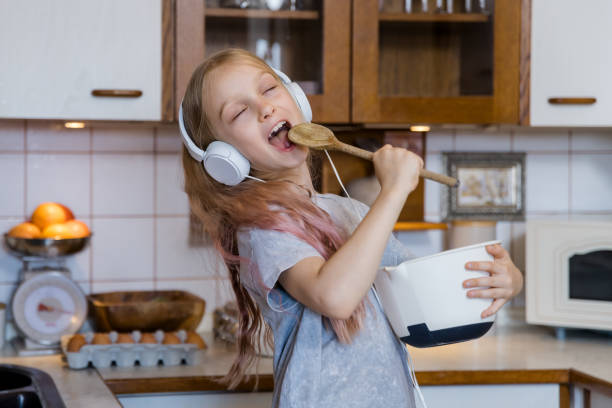 Little girl enjoying music while preparing food in kitchen Little girl listeing music in headphones and preparing food in kitchen making music stock pictures, royalty-free photos & images