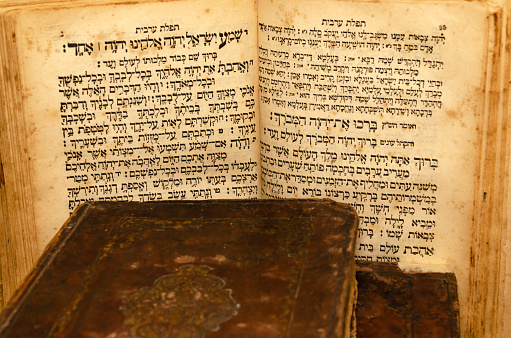 Stack of old and worn leather cover books with gold leaf embossing. Open book with text in Hebrew. Close-up.
