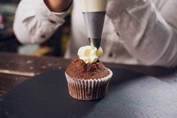 istock Woman making cream cheese top on cupcakes in kitchen. Cooking cakes. 1144221806