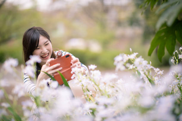 公共の公園でアイリスの花の写真を撮って幸せな若い女性 - iris single flower flower outdoors ストックフォトと画像