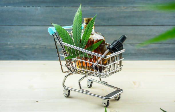 Supermarket trolley with marijuana leafs and medical cannabis oil cbd on wooden backdrop Supermarket trolley with marijuana leafs and medical cannabis oil cbd cannabis store photos stock pictures, royalty-free photos & images