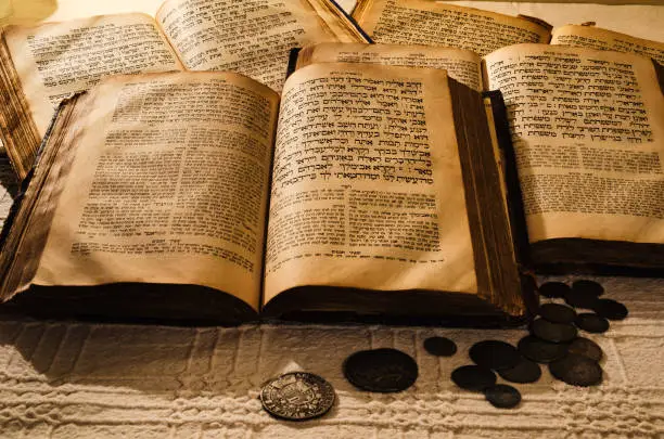 Pile of open old books in Hebrew and ancient coins scattered on the table. Linen tablecloth