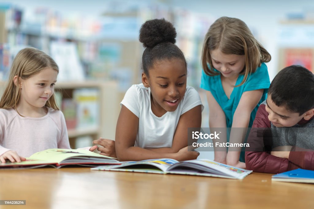 Children Reading A group of friends are sitting at a table in their classroom. They are reading a book together as they smile and laugh. Child Stock Photo