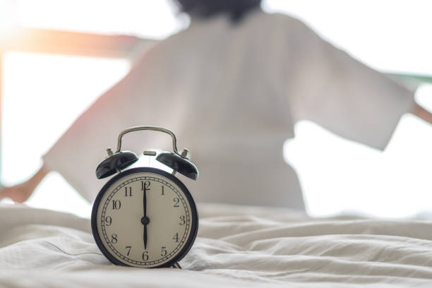 woman on bed wake up stretching in bedroom with alarm clock at 6.00 a.m. morning. biological clock healthcare concept. - 600 imagens e fotografias de stock