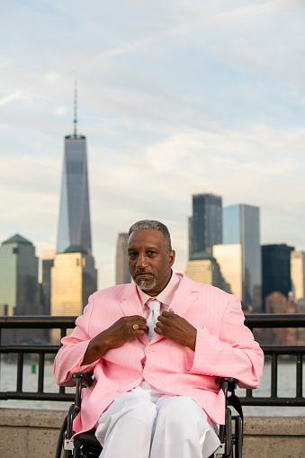 The positive, optimistic disabled wheel-chaired Afro-American Black veteran traveling in America, visiting Liberty State Park in New Jersey. Posing in front of Manhattan Downtown.