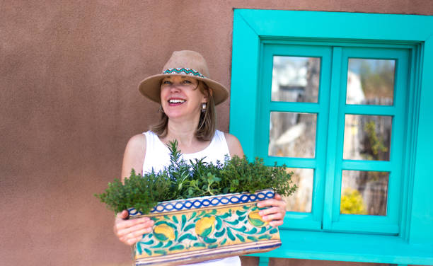 Plant Care: A woman in a sunhat holds a window box of herbs while standing next to a turquoise window (sill). Copy space available.