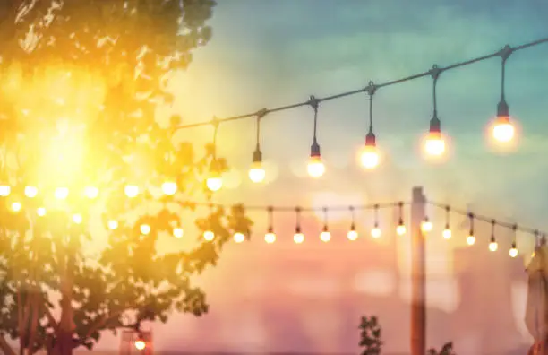 Photo of blurred bokeh light on sunset with yellow string lights decor in beach restaurant