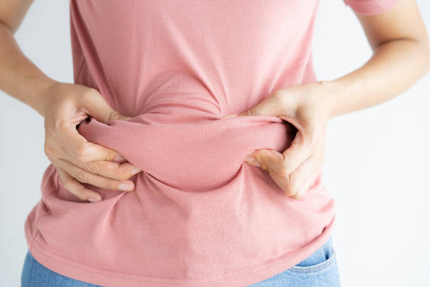 woman hand holding her own belly fat and cellulite on white background. women before weight loss and shape up healthy stomach muscle concept. - overweight imagens e fotografias de stock