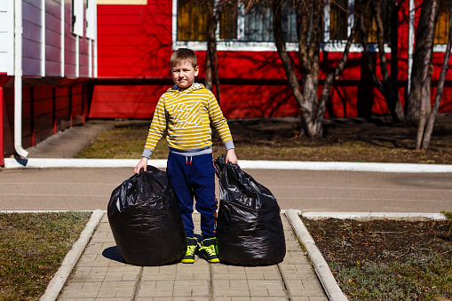 the child holds full garbage bags outdoors