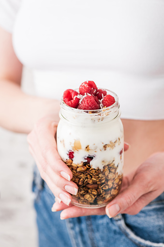 Yogurt parfait with granola and raspberries. Healthy breakfast in a jar. Sporty Woman hands holding healthy vegetarian, diet food