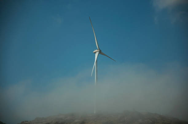 Wind turbines for electric power generation partially covered by mist over rocky hill, in a sunny day at Serra da Estrela. The highest mountain range in continental Portugal, with astonishing scenery.