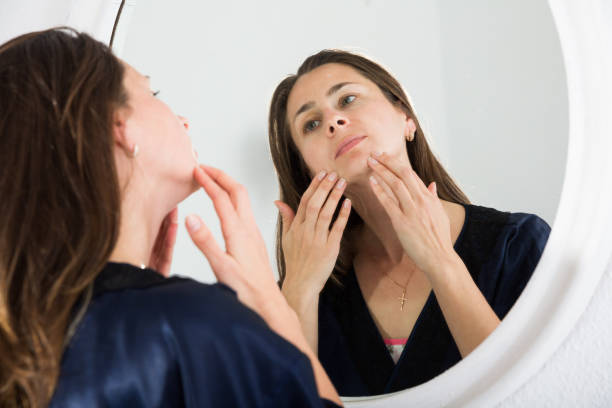 istock Young female touching face and looking at mirror in bedroom 1144279105