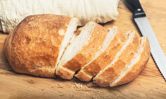 Ciabatta bread loaf slices on wooden board with knife. Fresh crusty white wheat bread Italian cuisine