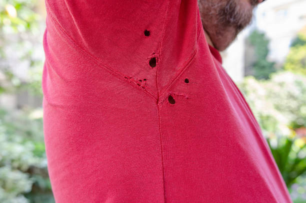 Bearded mature man raises his arm and opens holes in the armpit of a red old t shirt. stock photo