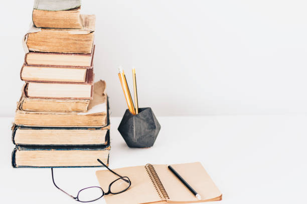 istock Stack of old books, textbook, notebook, glasses and pencils on white table in office background for education retro concept 1144280904