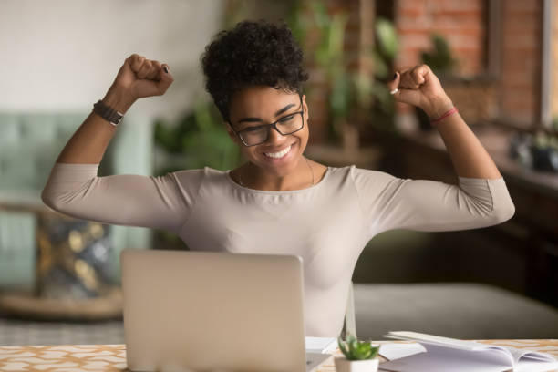 excitada mujer africana sintiendo ganador regocijo en línea ganar en el ordenador portátil - ladder of success fotografías e imágenes de stock