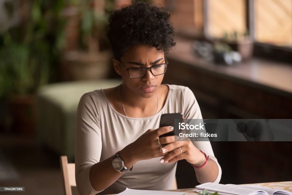 Upset confused african woman holding cellphone having problem with phone Upset confused african woman holding cellphone having problem with mobile phone, frustrated angry mixed race girl reading bad news in message looking at smartphone annoyed by spam or missed call White Collar Crime Stock Photo