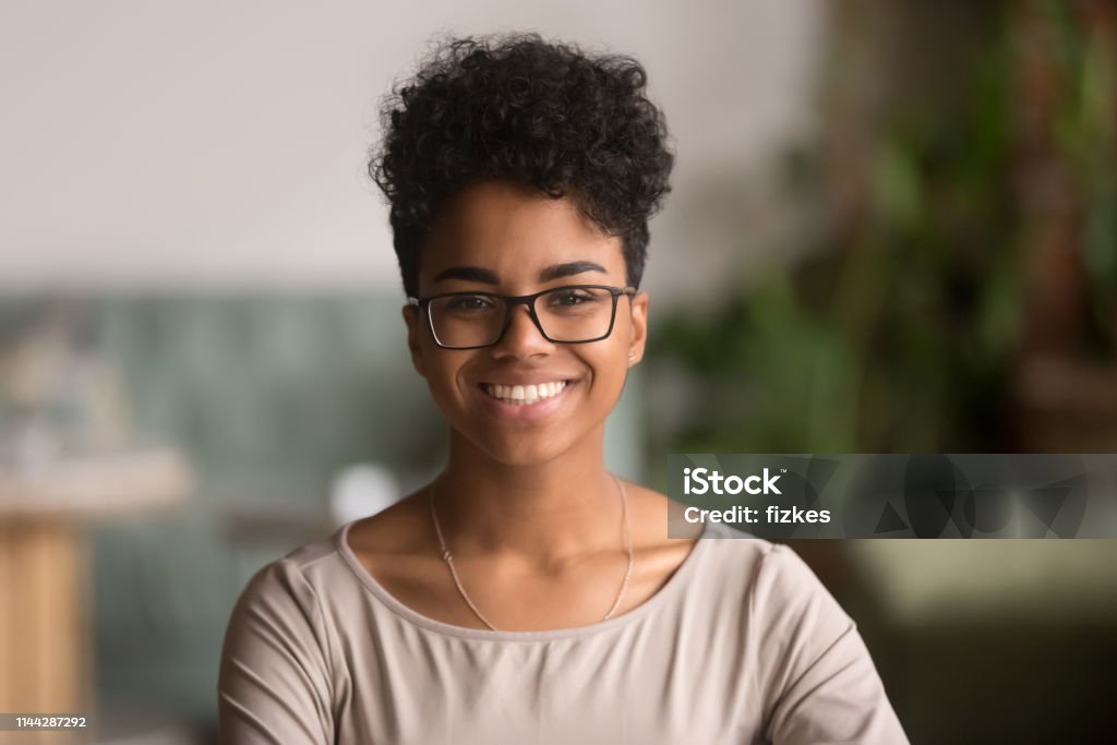 Headshot portrait of happy mixed race african girl wearing glasses Head shot portrait of happy mixed race girl wearing glasses, smiling african american millennial woman posing indoor, pretty positive female student businesswoman young professional looking at camera Women Stock Photo
