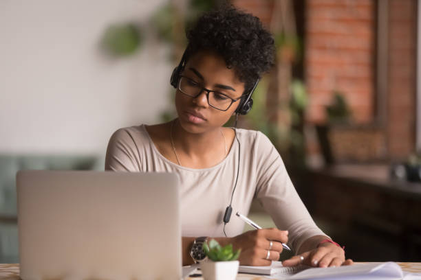 istock Focused mixed race woman wearing headphones watching webinar write notes 1144287296