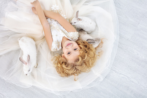 Little beautiful and cute girl in a trendy festive dress with animals rabbit in lies on the floor top view