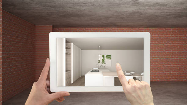 istock Augmented reality concept. Hand holding tablet with AR application used to simulate furniture and design products in interior construction site, modern kitchen with island and stools 1144289787