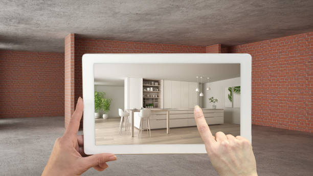istock Augmented reality concept. Hand holding tablet with AR application used to simulate furniture and design products in interior construction site, modern kitchen with island and stools 1144293715