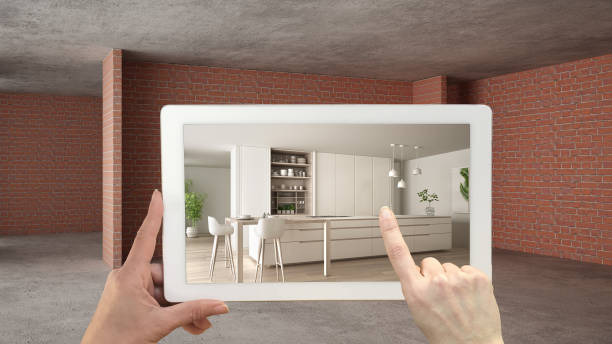 istock Augmented reality concept. Hand holding tablet with AR application used to simulate furniture and design products in interior construction site, modern kitchen with island and stools 1144296336