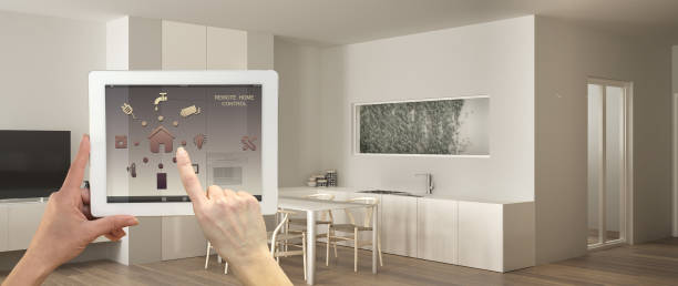 istock Smart remote home control system on a digital tablet. Device with app icons. Modern minimalist white kitchen with dining table in the background, architecture interior design 1144299460
